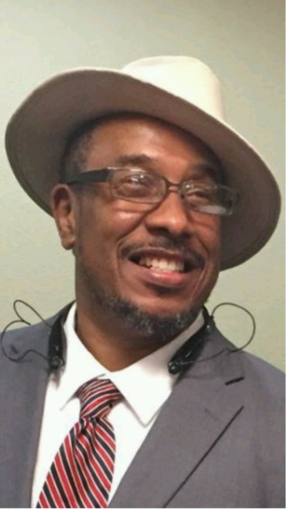 Headshot of Stancil Tootle, a Black man in a suit and tie wearing a hat cocked to the side. He has a mustache and glasses and is smiling while looking into the distance.