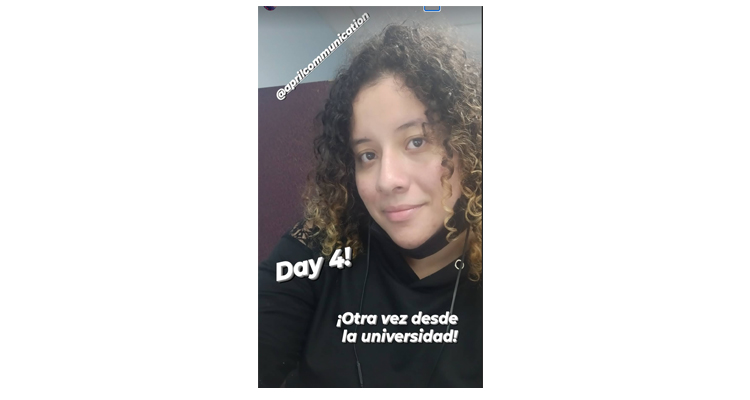 Screenshot of Kiara, a young woman with curly dark hair with blonder tips. Kiara is smiling with her mouth closed wearing a black hoodie. Text on photo says Day 4! Otra vez desde la universidad!