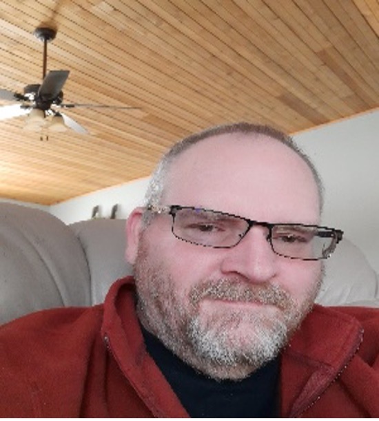 Hank Bostic, a white man with black rimmed glasses and short salt and pepper hair and facial hair relaxing at home in southwest Michigan, Winter 2021