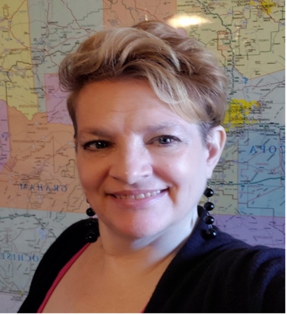 Mellie Santora, she/her/hers fair skinned, short blondish brown hair wearing black jacket and black earrings in front of a map of Arizona counties.